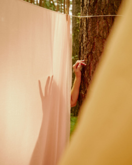 Hand reaching toward a tree trunk behind a pink sheet