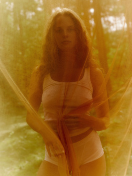 Woman in white underwear behind sheer orange-lit fabric