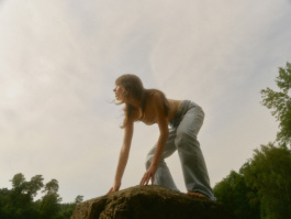 Woman crouching on a windswept boulder with hair across her chest