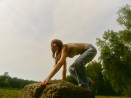 Woman crouching laughing atop a boulder in a field