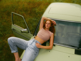 Woman leaning against a cream vintage van in a field