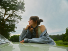 Woman resting her chin on hand atop a car hood