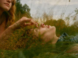 Two women lying in grass touching noses at golden hour