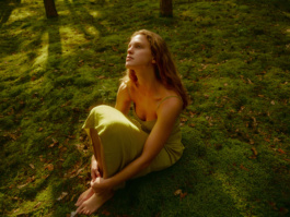 Woman sitting on moss hugging her knees in dappled light