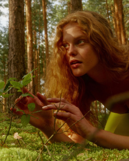 Woman lying on moss reaching for a green plant