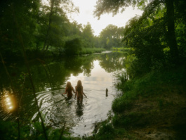 Two people wading into a forest river in golden light